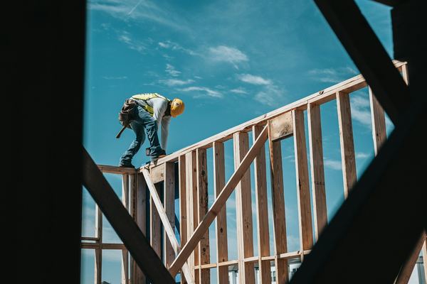 A builder working on timber wall framing against a blue sky