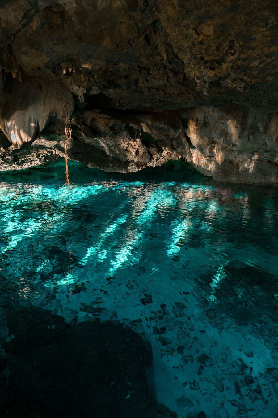 Turquoise water lit under an overhanging rock shelf.