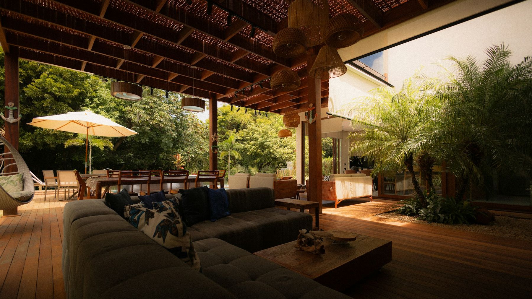 An open-air living room under a timber ceiling, opening onto garden and pool.